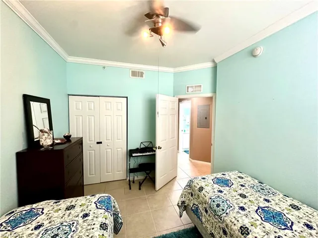 Bedroom featuring crown molding, light tile patterned floors, electric panel, ceiling fan, and a closet