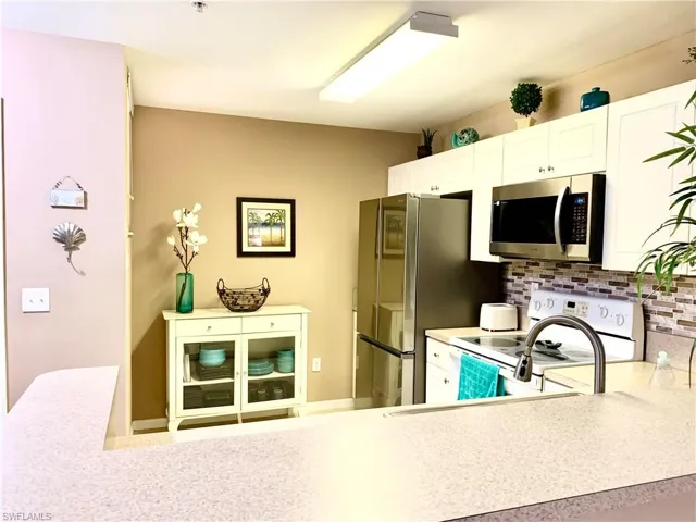 Kitchen featuring white cabinetry, stainless steel appliances, decorative backsplash, and kitchen peninsula