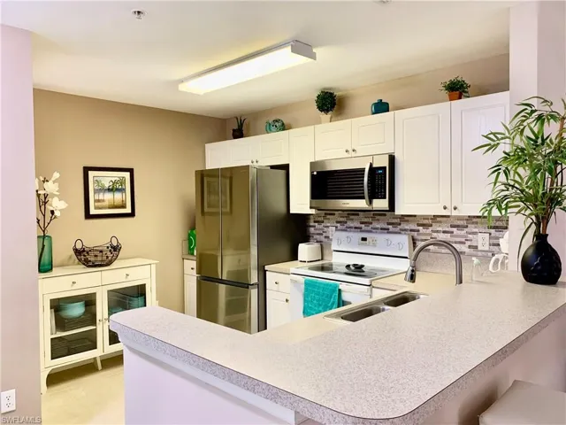Kitchen with appliances with stainless steel finishes, kitchen peninsula, tasteful backsplash, and light tile patterned floors