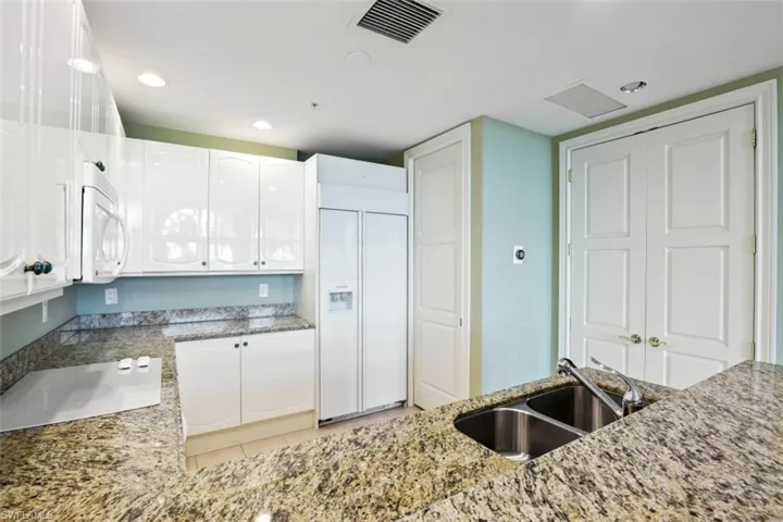 Kitchen featuring white microwave, a sink, paneled built in refrigerator, light stone counters, and white cabinets