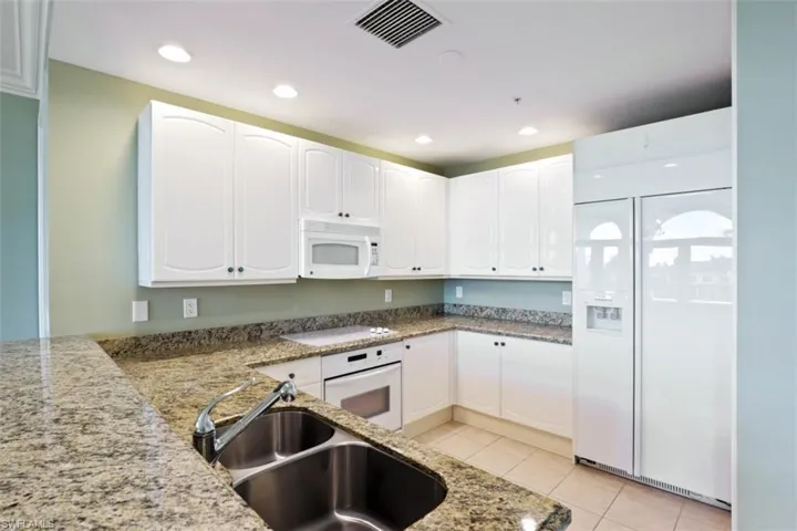Kitchen with white appliances, a sink, light stone counters, white cabinets, and light tile patterned floors