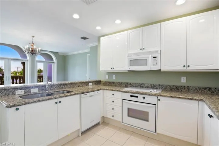 Kitchen featuring white appliances, a sink, dark stone countertops, white cabinets, and ornamental molding