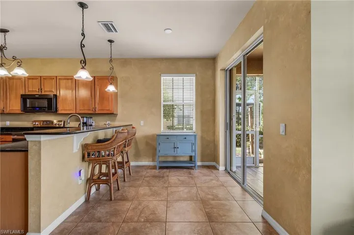 Kitchen featuring black microwave, dark countertops, hanging light fixtures, a kitchen breakfast bar, and a textured wall