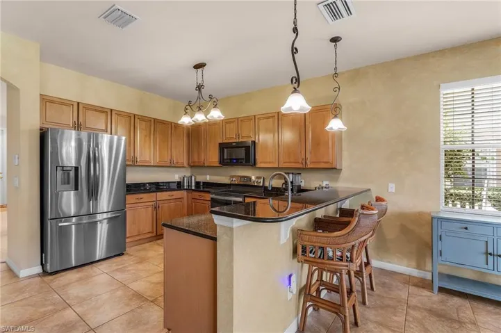 Kitchen with appliances with stainless steel finishes, a peninsula, a kitchen bar, light tile patterned floors, and decorative light fixtures