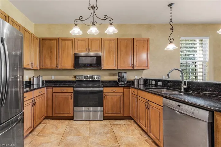 Kitchen with stainless steel appliances, brown cabinets, light tile patterned flooring, pendant lighting, and dark stone counters