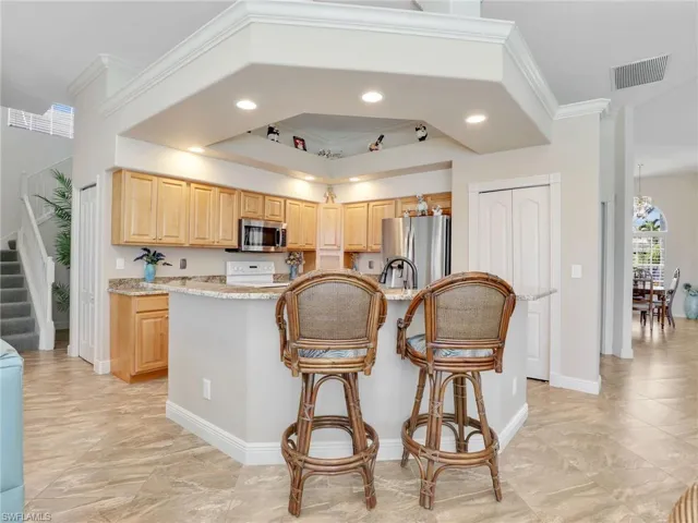 Kitchen with light brown cabinetry, ornamental molding, recessed lighting, a breakfast bar, and stainless steel appliances