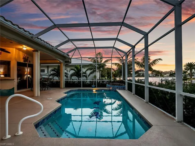 Pool at dusk with an outdoor pool, a sunroom, glass enclosure, and a patio