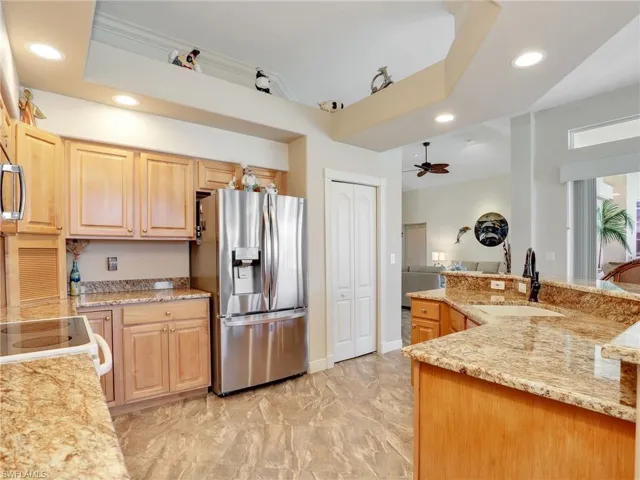Kitchen with recessed lighting, stainless steel refrigerator with ice dispenser, a ceiling fan, light stone counters, and light brown cabinetry