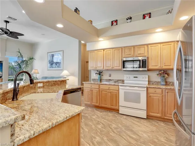 Kitchen with appliances with stainless steel finishes, recessed lighting, ornamental molding, light brown cabinetry, and light stone counters