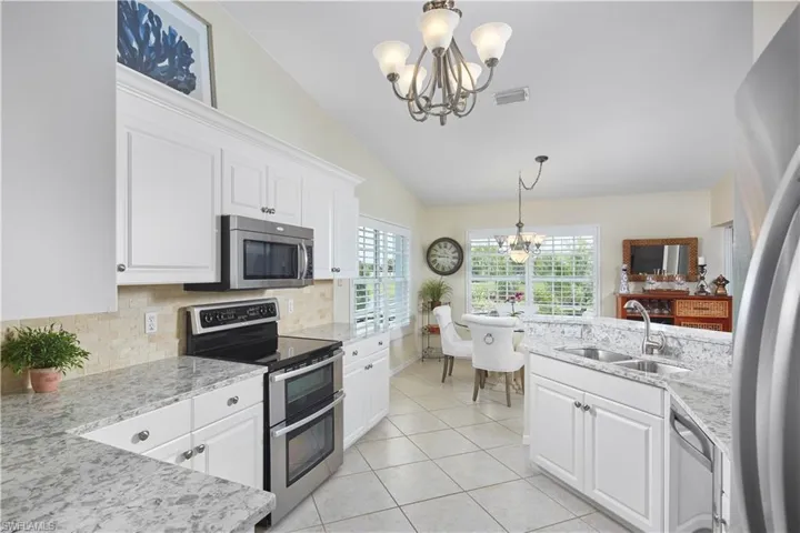 Kitchen featuring white cabinetry, lofted ceiling, stainless steel appliances, sink, and light tile flooring