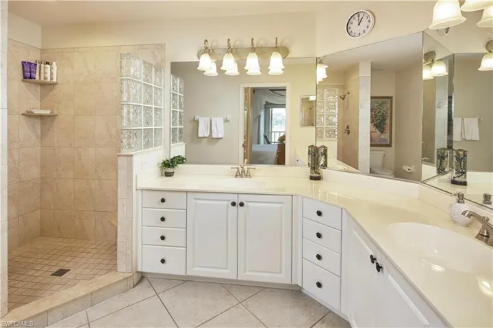 Bathroom with tiled shower, double sink vanity, tile flooring, and toilet