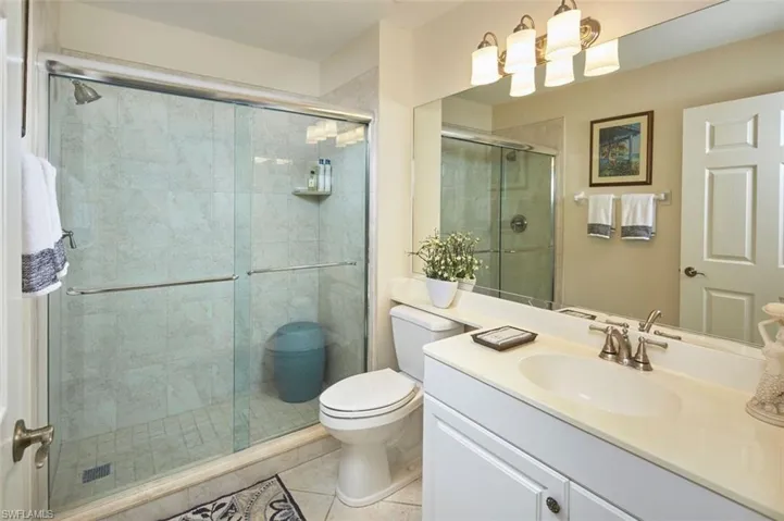 Bathroom featuring a shower with door, tile flooring, vanity, and toilet