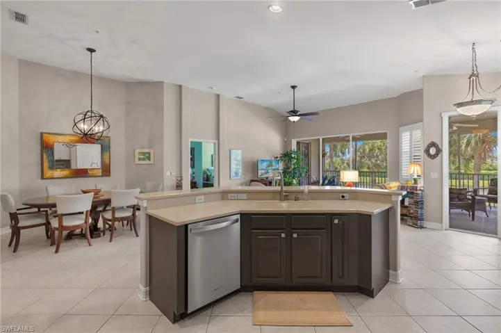 Kitchen with sink, a kitchen island with sink, stainless steel dishwasher, light tile patterned floors, and hanging light fixtures