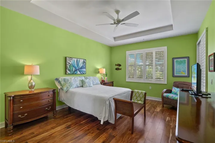 Bedroom with ceiling fan, a raised ceiling, and dark hardwood / wood-style floors