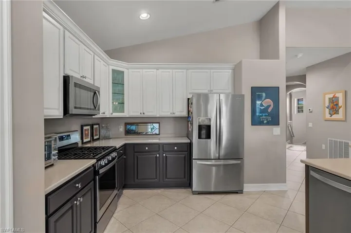 Kitchen featuring appliances with stainless steel finishes, white cabinets, light tile patterned floors, vaulted ceiling, and gray cabinets