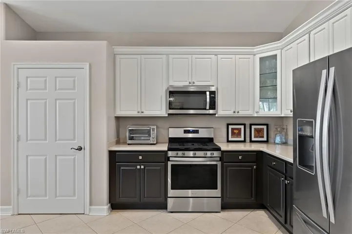 Kitchen featuring white cabinetry, light tile patterned floors, stainless steel appliances, and lofted ceiling
