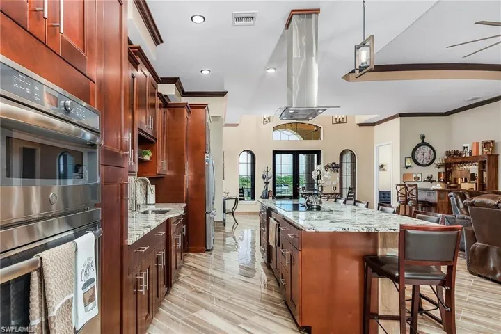 Kitchen featuring sink, double oven, a center island, light stone countertops, and island exhaust hood