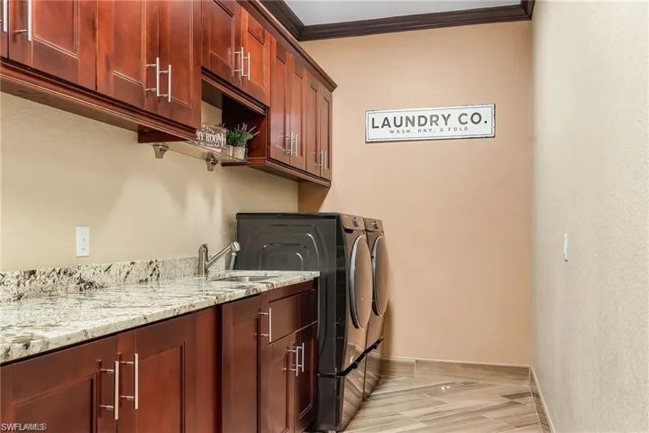 Laundry area with crown molding, cabinets, washer and clothes dryer, and sink