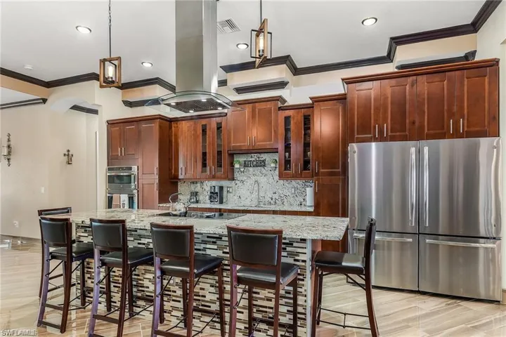 Kitchen with stainless steel appliances, light stone counters, island range hood, an island with sink, and a kitchen bar