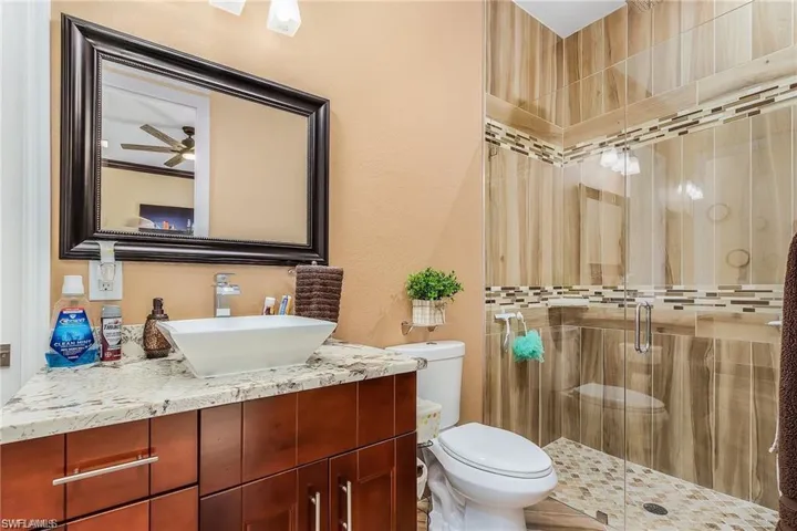 Bathroom featuring walk in shower, ceiling fan, vanity, and toilet
