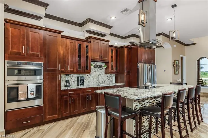 Kitchen with a breakfast bar area, appliances with stainless steel finishes, island exhaust hood, light stone countertops, and a kitchen island with sink