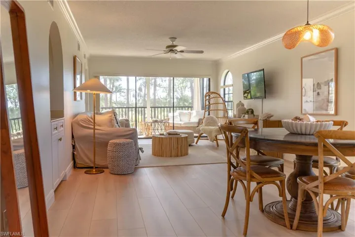 This living area features light-toned flooring, a ceiling fan, and large windows that provide views of the outdoors