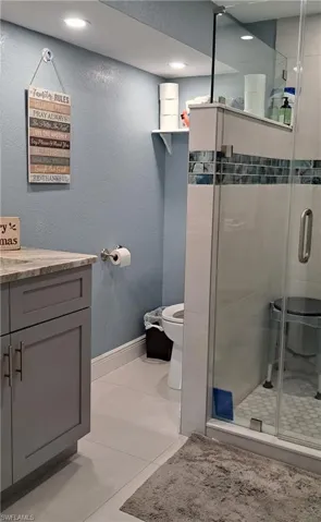 Bathroom featuring toilet, vanity, tile patterned floors, and a shower with shower door