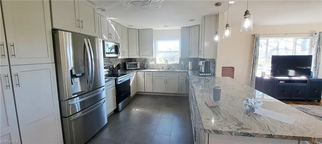Kitchen with a wealth of natural light, sink, stainless steel appliances, and hanging light fixtures