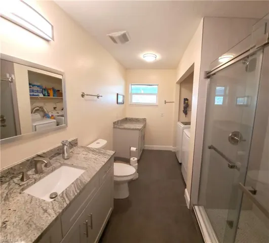 Bathroom featuring washer and clothes dryer, vanity, toilet, and walk in shower
