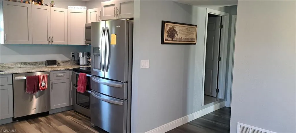 Kitchen featuring appliances with stainless steel finishes, gray cabinets, dark hardwood / wood-style floors, and light stone counters