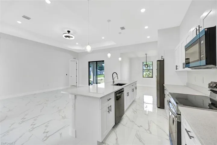 Kitchen featuring light stone counters, stainless steel appliances, a sink, white cabinetry, and pendant lighting