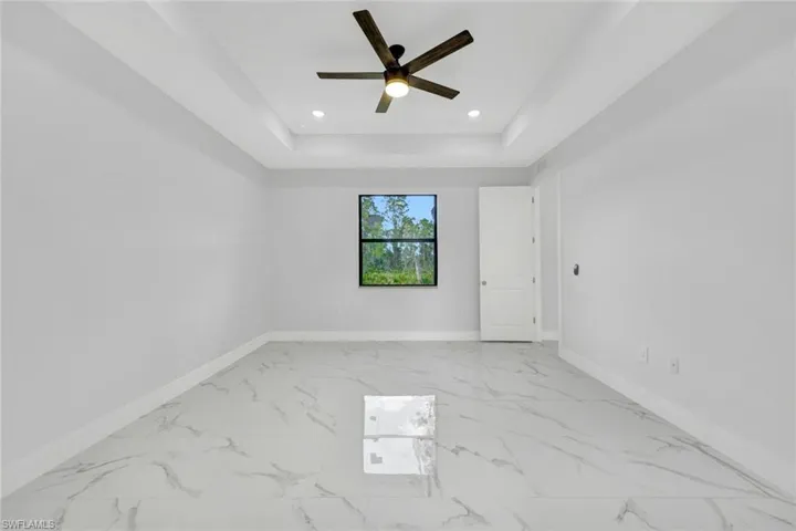 Unfurnished room with baseboards, a raised ceiling, a ceiling fan, marble finish floor, and recessed lighting