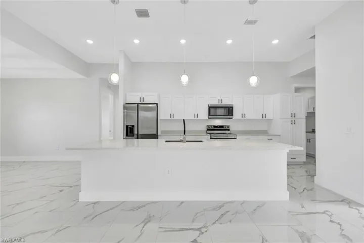 Kitchen featuring a spacious island, light stone counters, appliances with stainless steel finishes, pendant lighting, and a sink