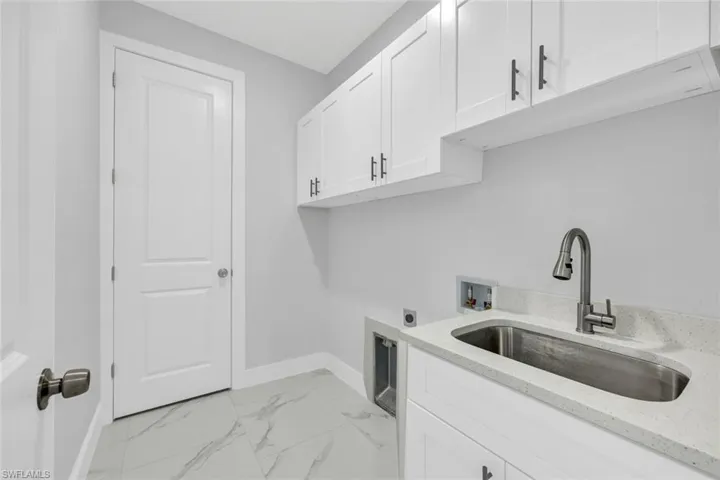 Washroom with cabinet space, a sink, hookup for a washing machine, marble finish floor, and electric dryer hookup