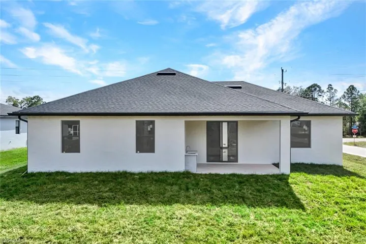 Back of house with a yard, a patio area, and roof with shingles