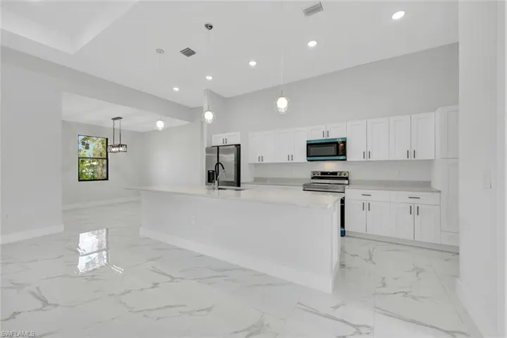 Kitchen featuring stainless steel appliances, hanging light fixtures, a center island with sink, and white cabinets