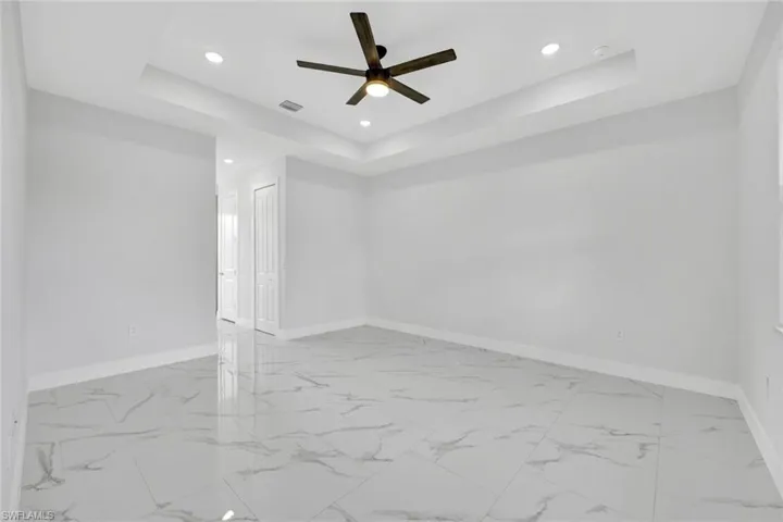 Empty room featuring ceiling fan, recessed lighting, visible vents, baseboards, and a tray ceiling