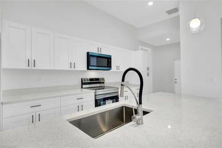 Kitchen featuring electric stove, light stone counters, a sink, and white cabinets
