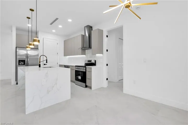 Kitchen featuring stainless steel appliances, wall chimney range hood, modern cabinets, recessed lighting, and decorative light fixtures