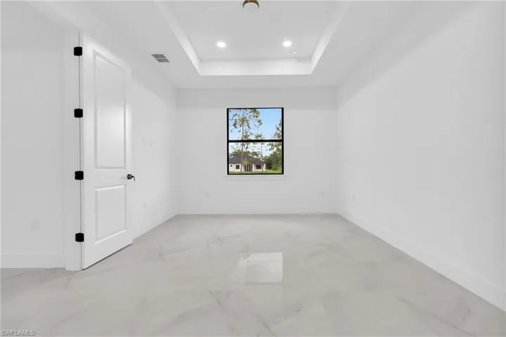 Empty room with light marble finish floors, a tray ceiling, and recessed lighting