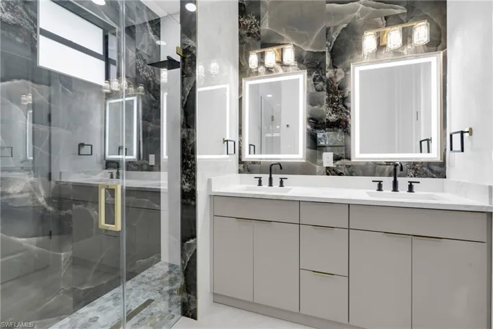 Full bath with double vanity and a marble finish shower