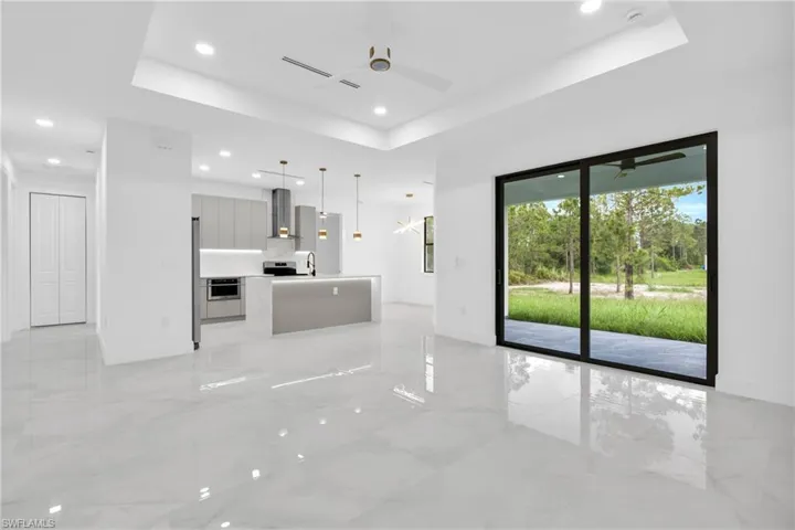 Unfurnished living room with a tray ceiling, recessed lighting, ceiling fan, and light marble finish floors
