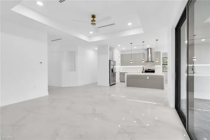 Unfurnished living room with ceiling fan, a raised ceiling, recessed lighting, and light marble finish floors