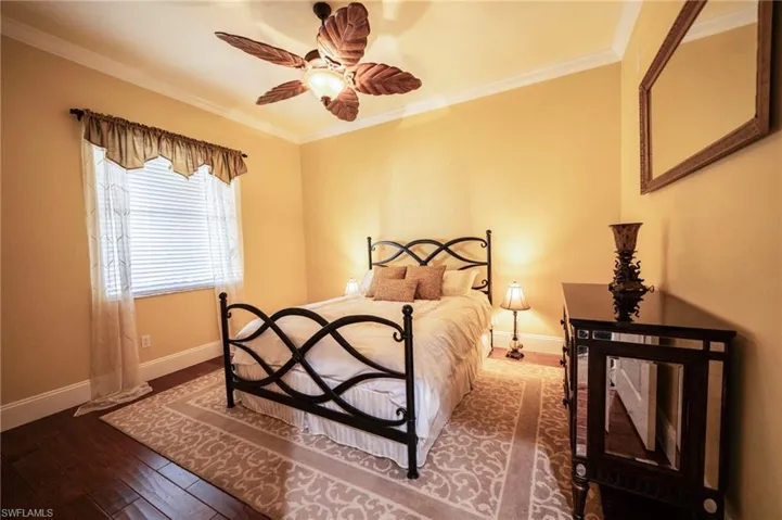 Bedroom with dark hardwood / wood-style flooring, crown molding, and ceiling fan