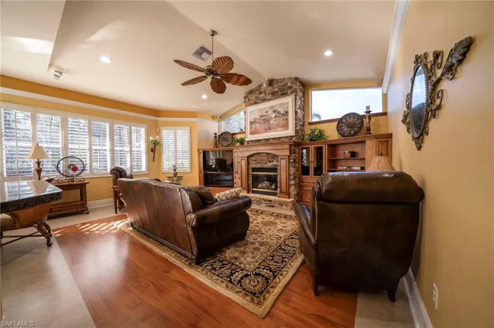 Living room featuring lofted ceiling, a stone fireplace, ornamental molding, hardwood / wood-style flooring, and ceiling fan