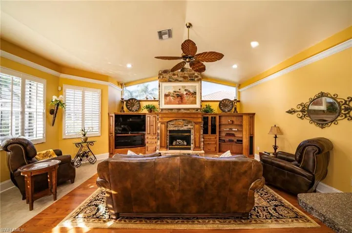 Living room featuring ceiling fan, lofted ceiling, ornamental molding, and a fireplace
