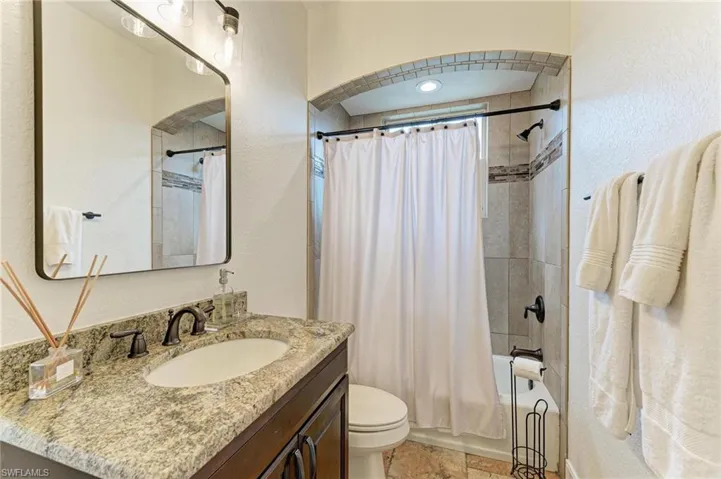 Full bathroom with vanity, shower / bath combo with shower curtain, and a textured wall