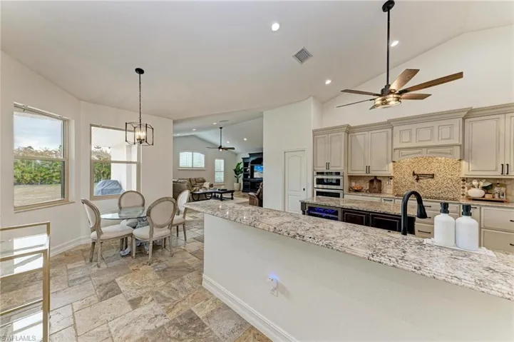 Kitchen featuring ceiling fan, lofted ceiling, light stone counters, stone tile floors, and tasteful backsplash