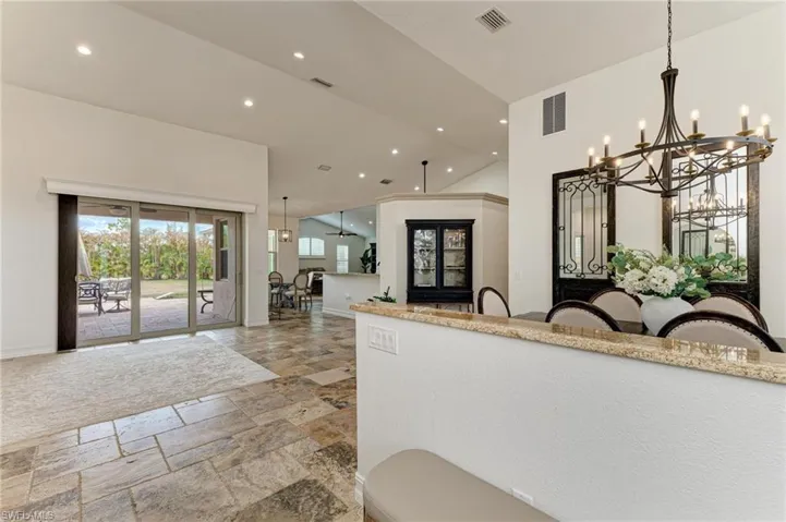 Kitchen with stone tile flooring, a chandelier, light stone counters, lofted ceiling, and open floor plan