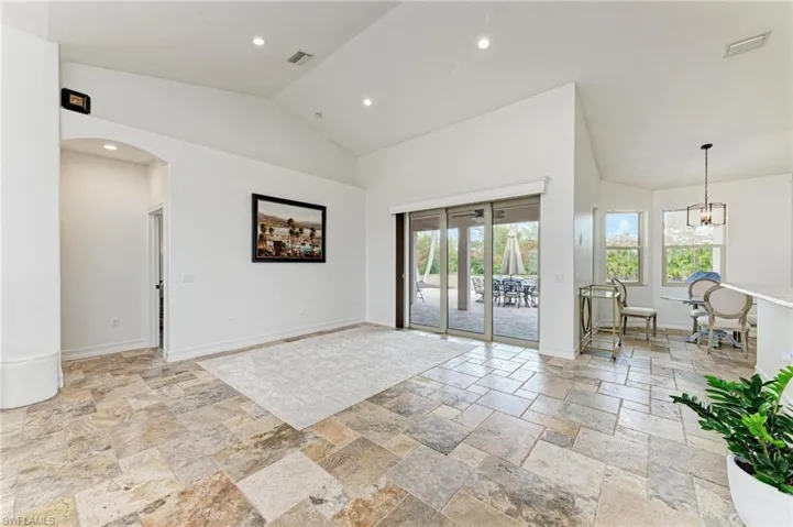 Unfurnished room with lofted ceiling, arched walkways, hanging lights, and stone tile flooring